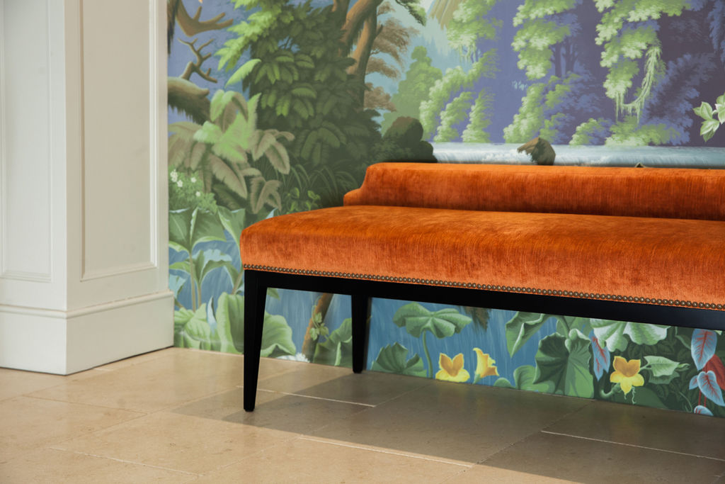Ochre velvet bench against scenic mural wallpaper in a classical interior hallway.